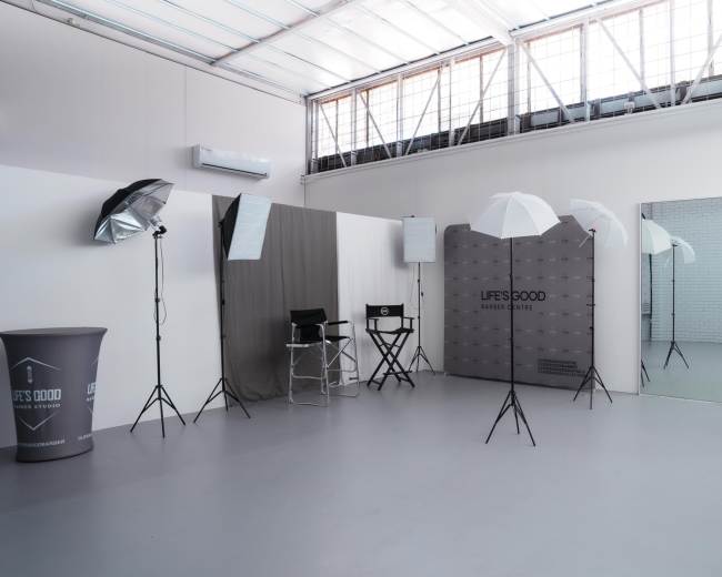 The image shows a photography studio equipped with lighting equipment, a director's chair, and a large mirror against a minimalist backdrop.