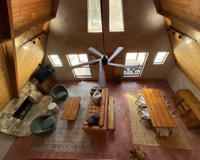 The image shows an aerial view of a spacious, modern living area featuring a wooden dining table, a leather sofa, and large windows allowing natural light to illuminate the space.
