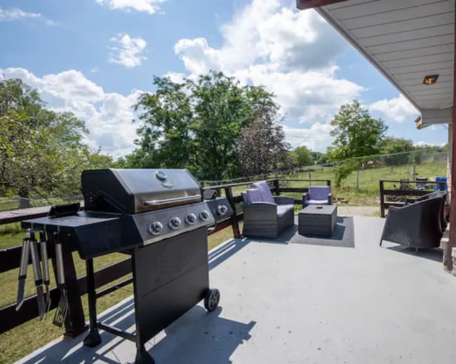 A patio features a barbecue grill and outdoor seating, with a view of trees and a grassy area beyond.