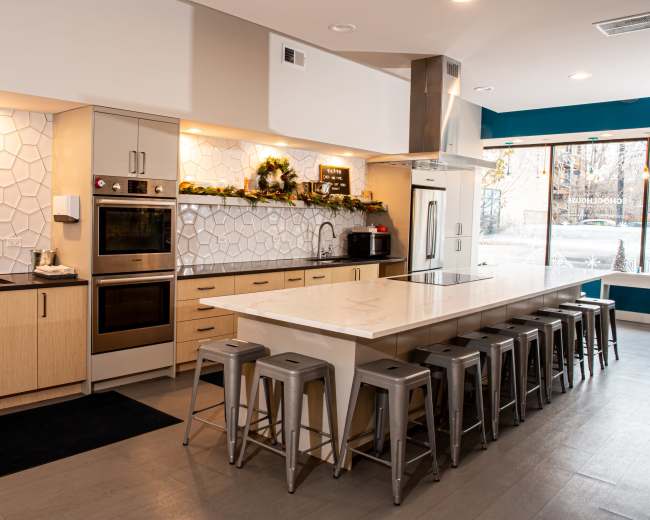 A modern kitchen with a large island and metal bar stools, featuring light wood cabinetry and a patterned backsplash.