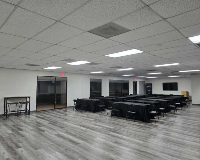 The image shows a spacious meeting room with black tables arranged in rows and large windows on one side.