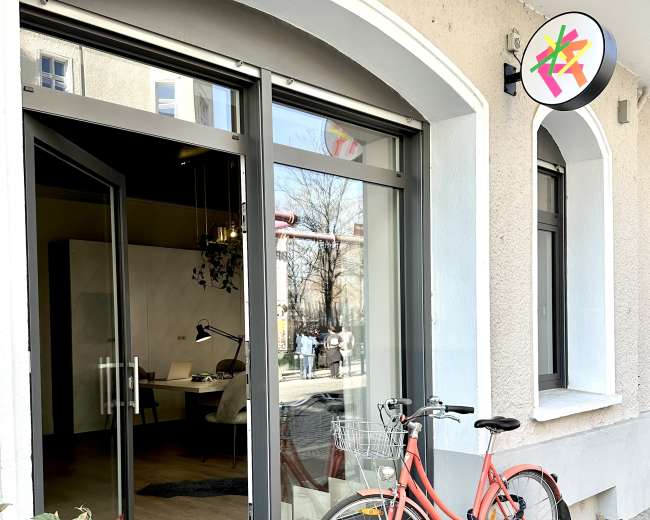 A red bicycle is parked next to an open storefront with large glass doors and a circular sign above.