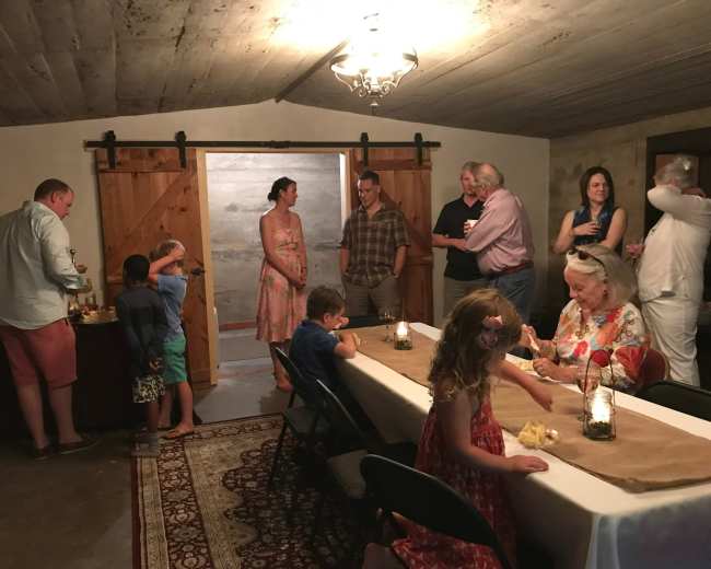 A group of people are gathered in a room with wooden doors, socializing and enjoying snacks around a long table with lanterns.
