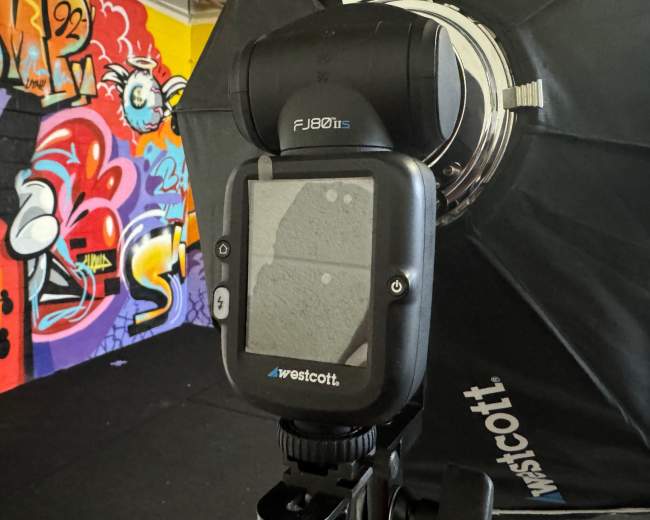 A Westcott flash unit is positioned in front of a colorful graffiti wall in an indoor setting.