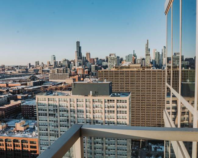 A modern living room features a large window showcasing a city skyline, with a black sofa, a round chair, and a shaggy rug.