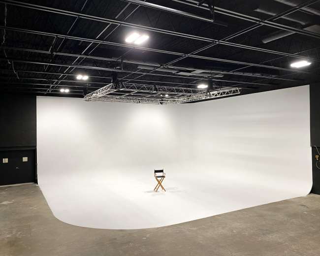 A large, empty photography studio with a smooth white backdrop and a single director's chair positioned in the center.