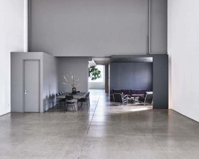 The image displays a spacious, modern interior with a grey color palette, featuring a dining area with a table and chairs on one side and a seating area with a sofa on the other.