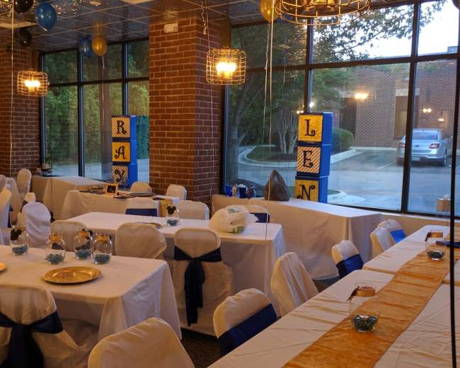 A decorated event space with tables covered in white linens and blue accents, arranged for a celebration.