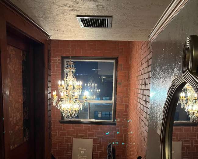 A staircase leading down to a lower level, with a chandelier and a decorative mirror visible on the walls.