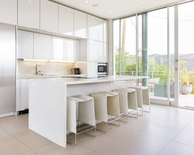 The image shows a modern kitchen with white cabinetry, stainless steel appliances, and a long island with six stools.