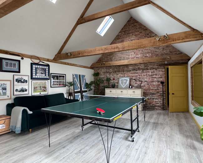 A game room featuring a ping pong table, exposed brick walls, wooden beams, and a green door.