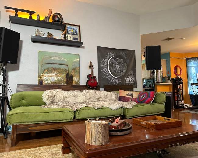 The image shows a living room with a green couch, a wooden coffee table, and various decorations, including speakers and a guitar on the wall.