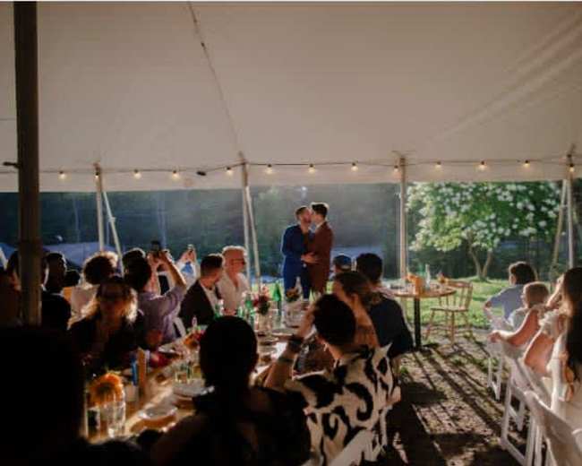A couple shares a dance under a tent filled with seated guests enjoying a meal in a well-lit outdoor setting.