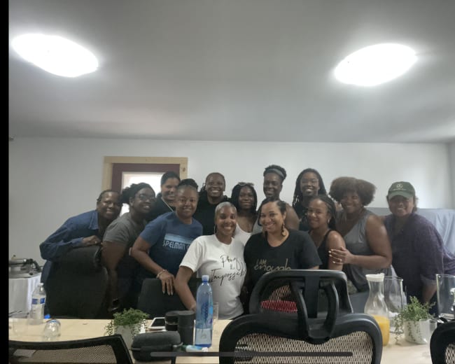 A group of fifteen individuals poses together in a well-lit room with a long table.