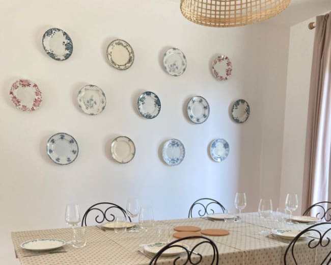 A dining table set with plates and glasses is arranged under a wall decorated with various patterned plates.