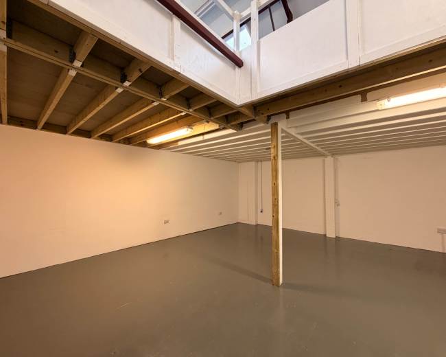 The image shows a spacious, empty basement area with a wooden support column and a mezzanine level above.