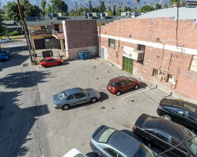 The image shows a mostly empty parking lot adjacent to a brick building, with several parked cars and a dumpster visible.