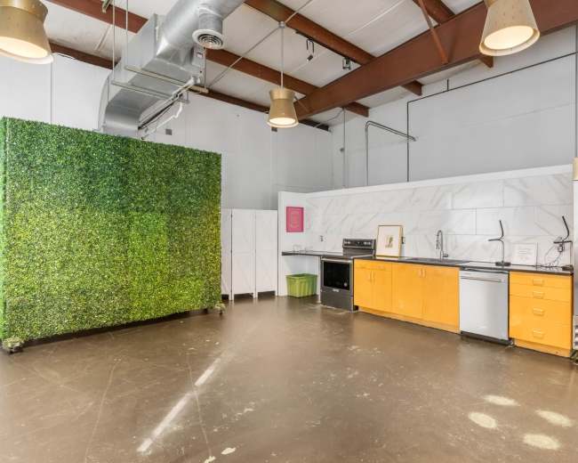 The image shows a modern kitchen area featuring a green plant wall, stainless steel appliances, and light wood cabinetry.