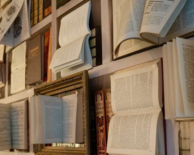 A wall displays an arrangement of various books, with some pages opened and others stacked vertically.