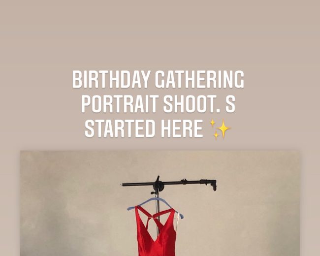 A red dress is hung on a clothing rack against a plain backdrop in a portrait studio setting.