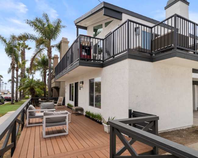 A two-story white house with a balcony, palm trees nearby, and an American flag flying above.