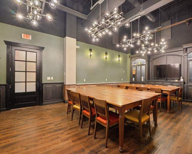 The image shows a conference room with a long wooden table surrounded by chairs and modern chandelier lighting above.