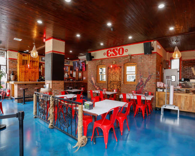 The image shows a restaurant interior with red chairs, wooden accents, and a bar area.