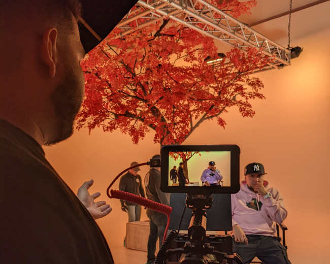 A photographer captures an individual seated in front of a large artificial tree in a studio setting.