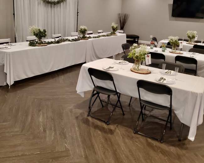 A banquet room is set up with white tablecloths, chairs, and decor, including small floral centerpieces.
