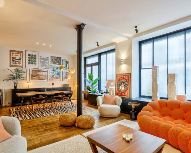 The image showcases a modern living space with a mix of seating arrangements, large windows, and vibrant artwork on the walls.