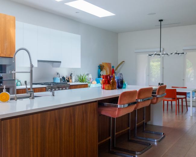 A modern kitchen with a large island, wooden cabinetry, and colorful glassware displayed on the countertop.