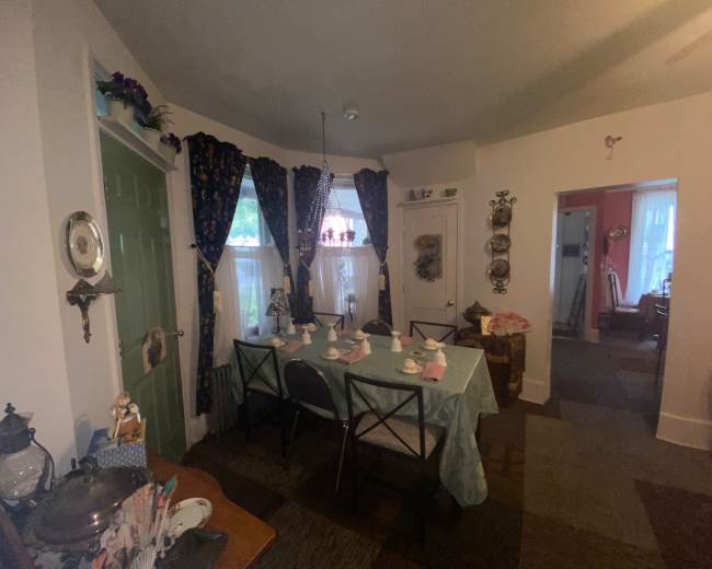 The image shows a dining area with a long table set for a meal, surrounded by decorated walls and doorways leading to other rooms.