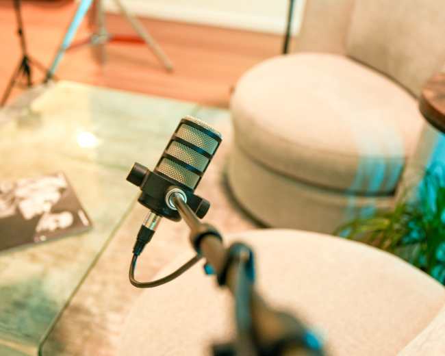 A microphone stands on a table next to a magazine and a pair of empty chairs in a cozy room setting.