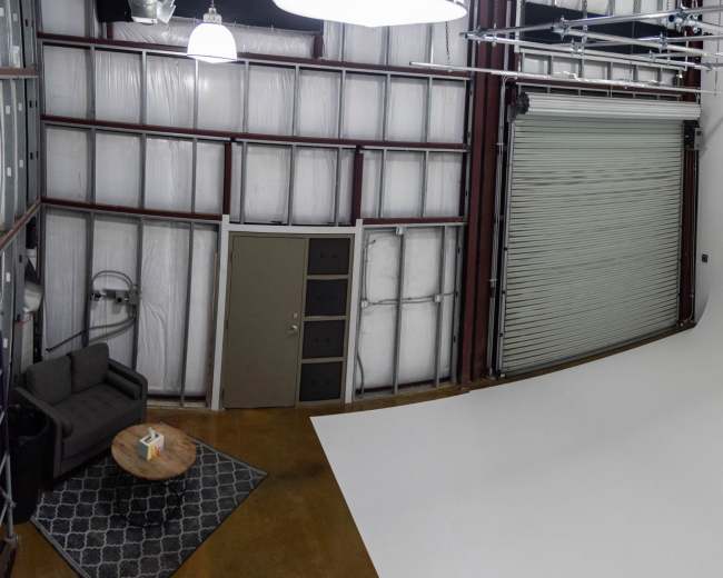 A spacious studio features a large white backdrop and a seating area with a coffee table.