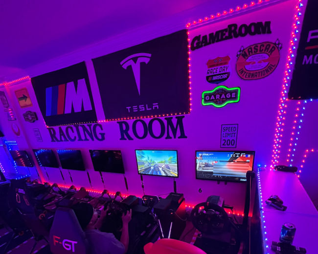 The image shows a vibrant racing simulation room with multiple screens, gaming chairs, and neon lighting.