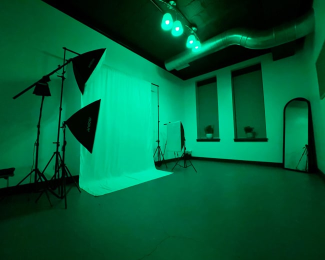 A photography studio with green lighting, featuring a draped backdrop, lighting equipment, and a large mirror.