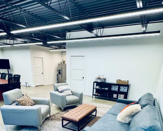 The image shows a modern office lounge area with two armchairs, a sofa, a coffee table, and a large area rug.