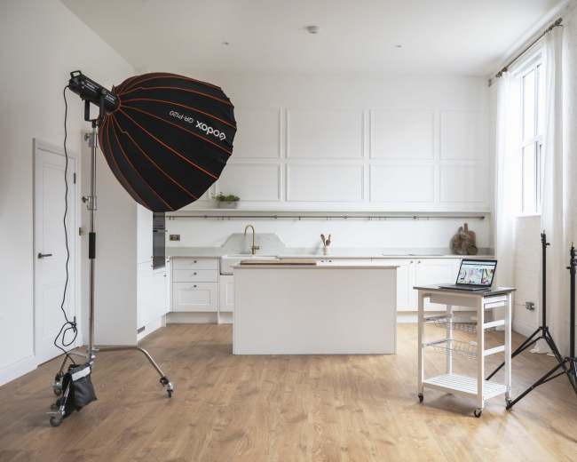 A modern kitchen with white cabinetry, a central island, and a photography lighting setup on the side.
