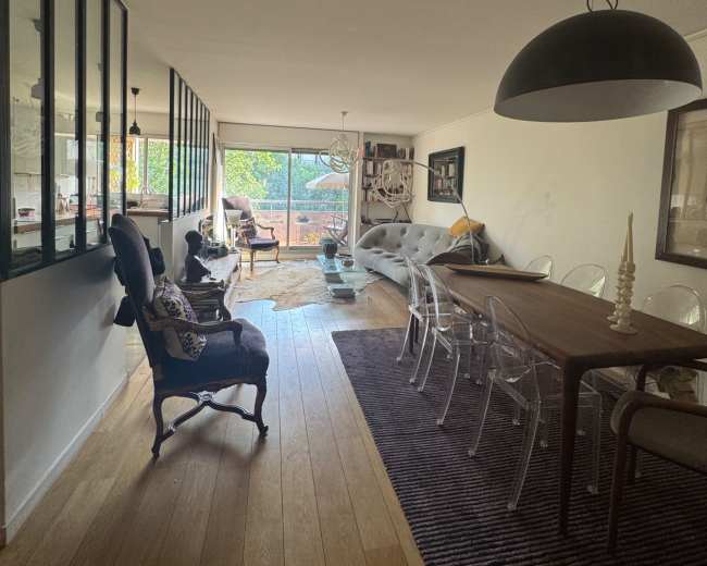 The image shows a modern open-concept living and dining area with large windows, hardwood flooring, and a mix of contemporary and classic furniture.