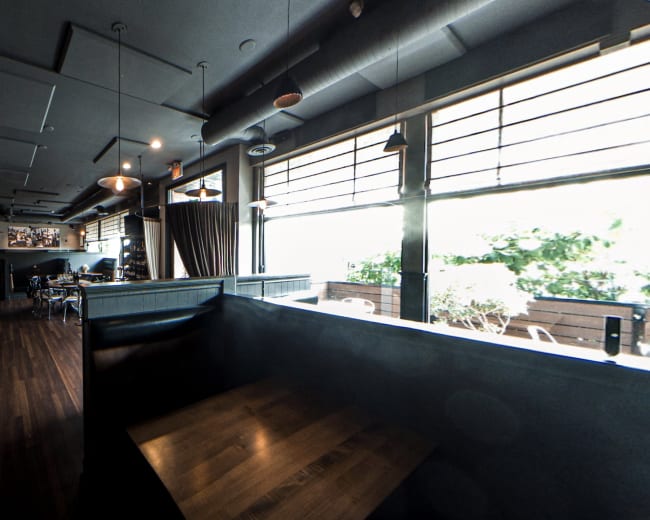 A modern restaurant interior with wooden tables, a bar area, and large windows allowing natural light to enter.