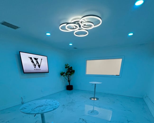 The room features a glossy marble floor, two circular tables, a large screen displaying a logo, and modern lighting, all in a blue-toned color scheme.