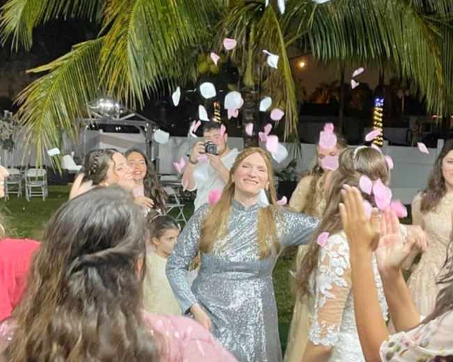 A group of people dance in a lush outdoor setting while petals fall around them.