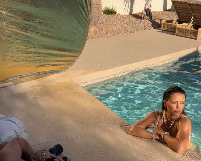 A photographer captures a model leaning gracefully by a pool while using a reflector for lighting.