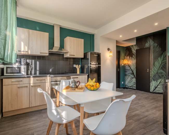 A modern kitchen features wooden cabinets, a black refrigerator, and a dining table with white chairs, surrounded by green palm-patterned wallpaper.