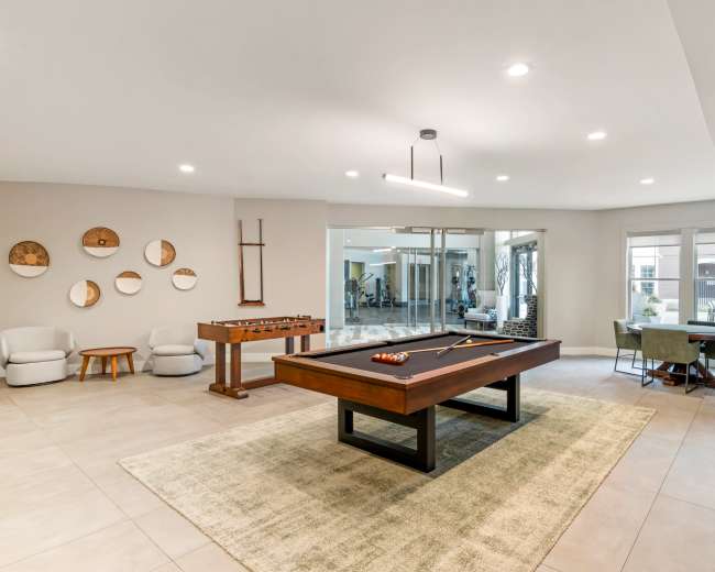 The room features a pool table, foosball table, seating area, and a large window overlooking an outdoor space.