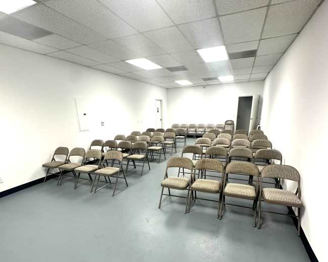 A spacious room is set with several rows of empty metal chairs arranged neatly on a gray floor.