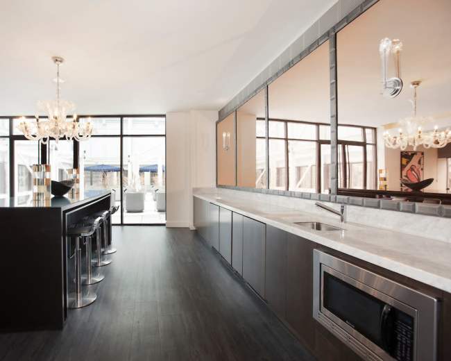 The image shows a modern kitchen with a linear layout featuring a bar, sleek cabinetry, and large windows that provide ample natural light.