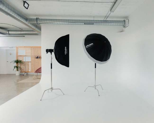 The image shows a brightly lit photography studio featuring two light umbrellas on stands and a seamless white backdrop.