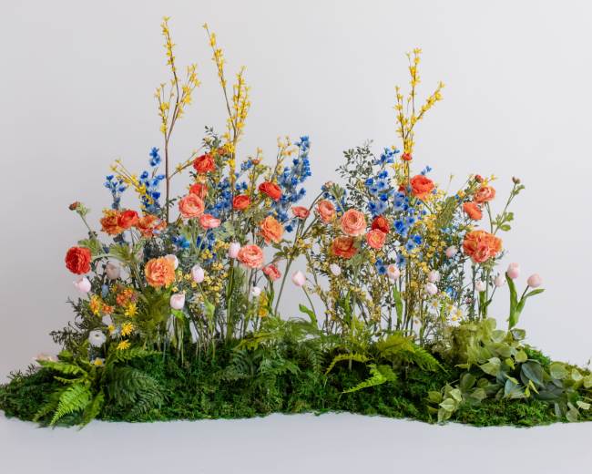 A vibrant arrangement of various flowers and greenery is displayed on a white background.