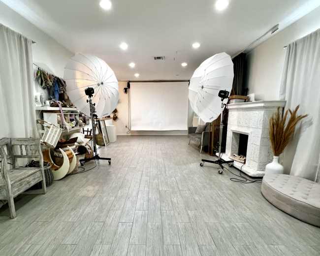 The image shows an empty studio space with a backdrop, two lighting setups, a decorative fireplace, and various props arranged along one wall.